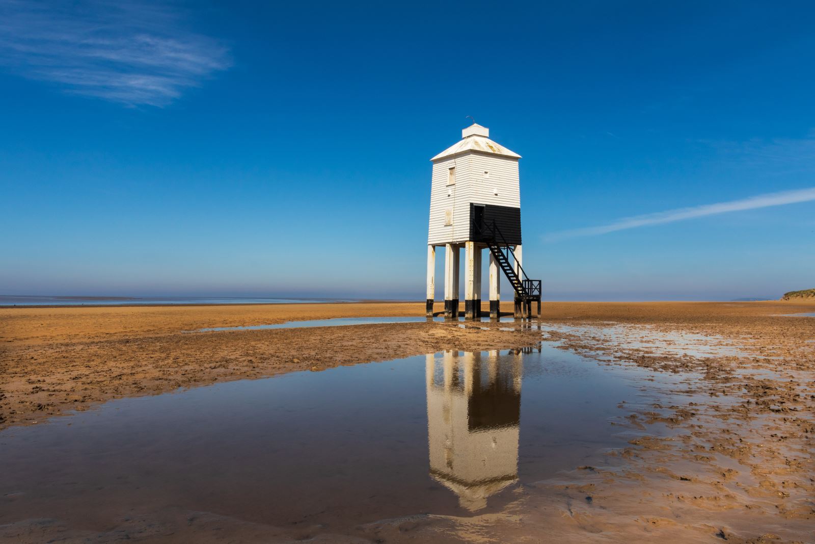 Burnham-On-Sea's Low Lighthouse reflected in a puddle on the sandy beach. The lighthouse is built on nine stilts