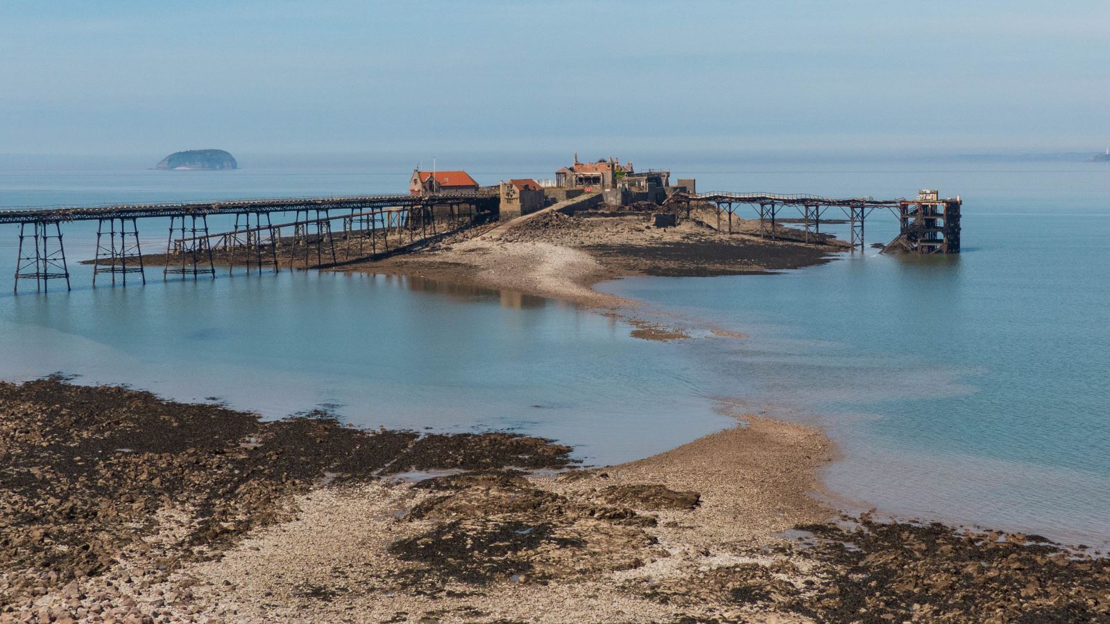 Aerial view of a decaying pier on an island with a causeway leading to it