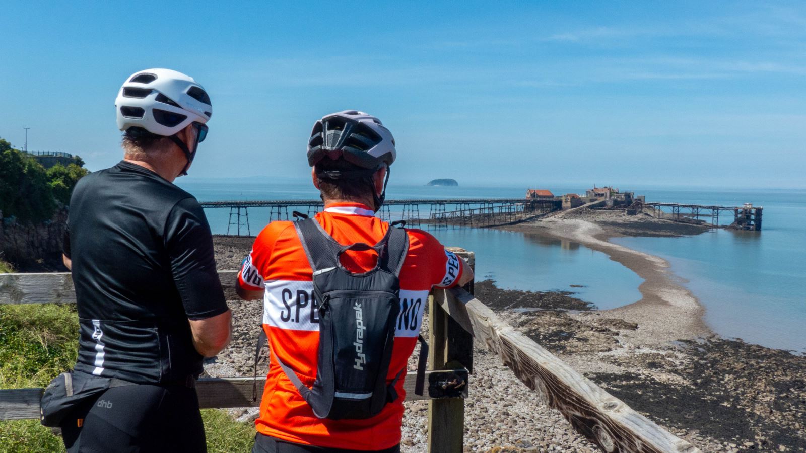 Two cyclists with helmets on admire a sea view