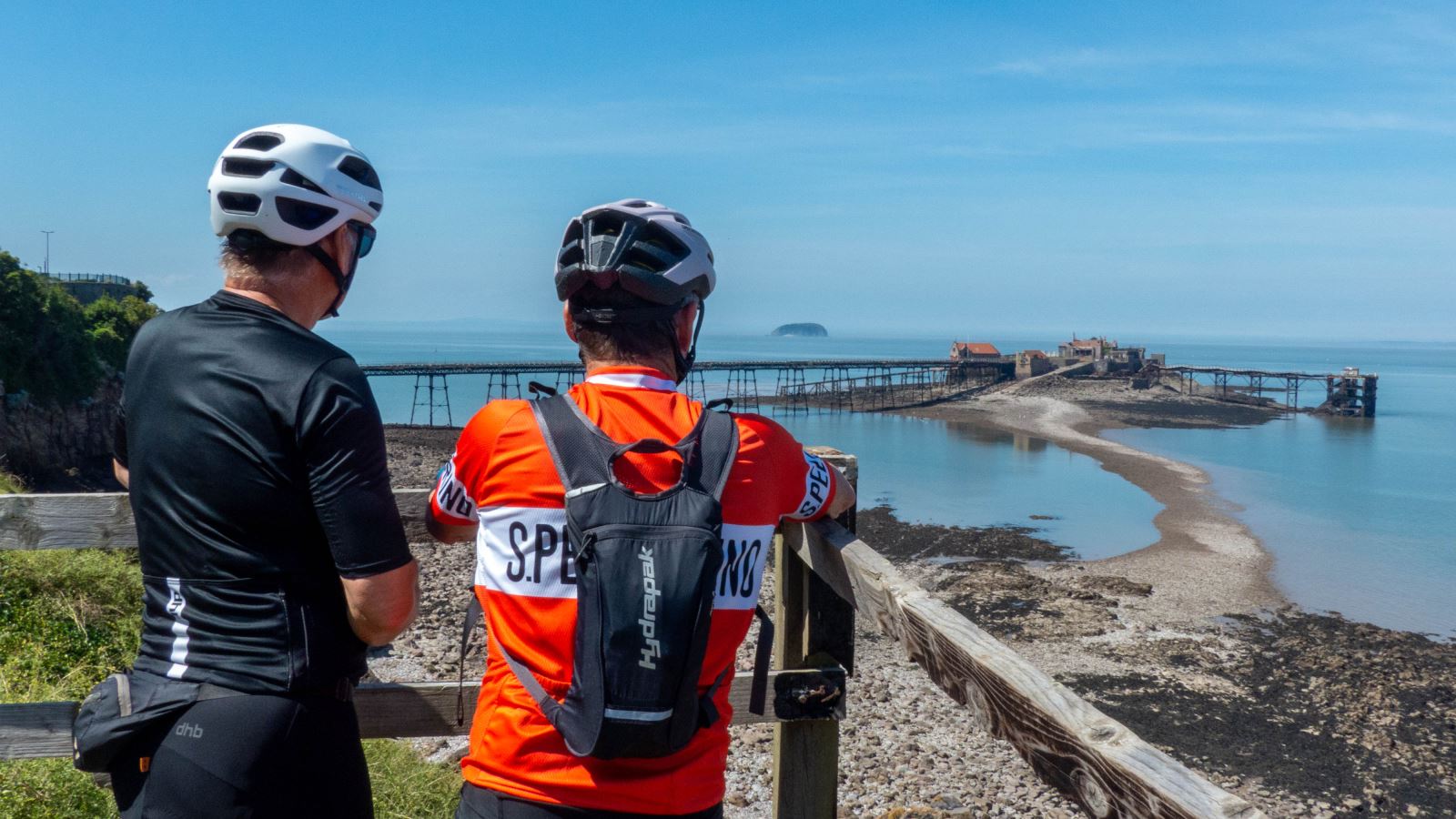 Two cyclists leaning on a fence admiring a sea view