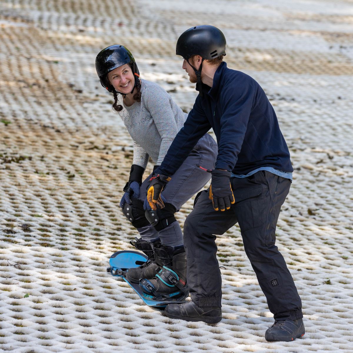 A lady receiving a snowboard lesson from a male instructor at the Mendip Activity Centre